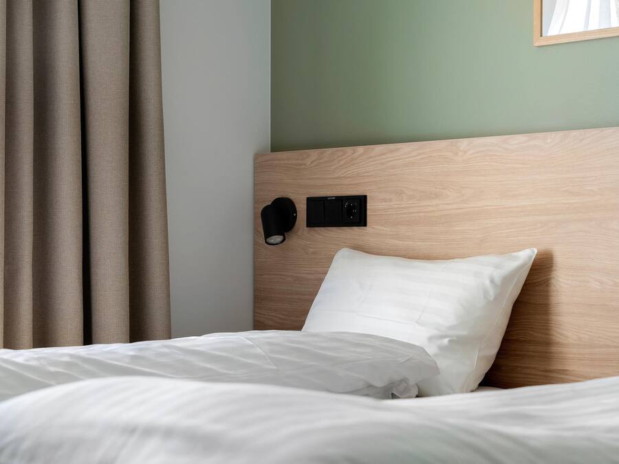 Una cama bien hecha con ropa de cama blanca, cabecera de madera y panel de control en la pared.