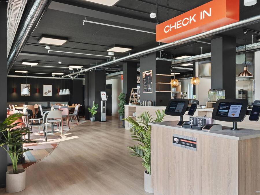 Un área de recepción moderna con mostrador, zona de estar y un cartel que indica 'CHECK IN'.