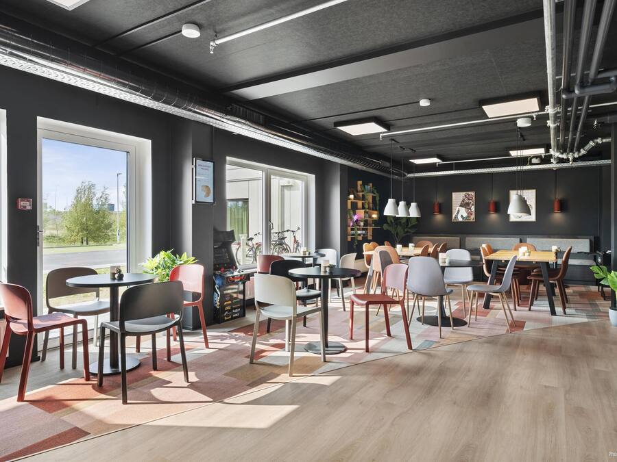 A modern cafe with multiple seating areas, large windows, and indoor plants.