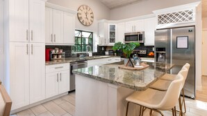 Una cocina moderna con armarios blancos, encimera de granito, electrodomésticos de acero inoxidable y un reloj grande.