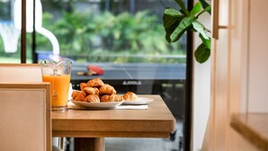 Una mesa de desayuno con cruasanes y jugo de naranja, una planta y vistas de vegetación al exterior.