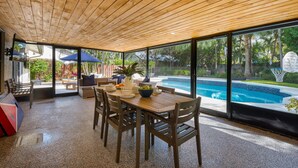 Amplio espacio interior con techo de madera, ventanas grandes, piscina y zona de estar exterior.