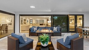 A modern outdoor living area with a fire feature, wicker furniture, and a view into the house. - Boynton Beach Retreat, Close to Delray, Aug Deal (Boynton Beach)