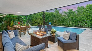 A poolside area with a fire pit, seating, and a view of lush greenery. - Boynton Beach Retreat, Close to Delray, Aug Deal (Boynton Beach)