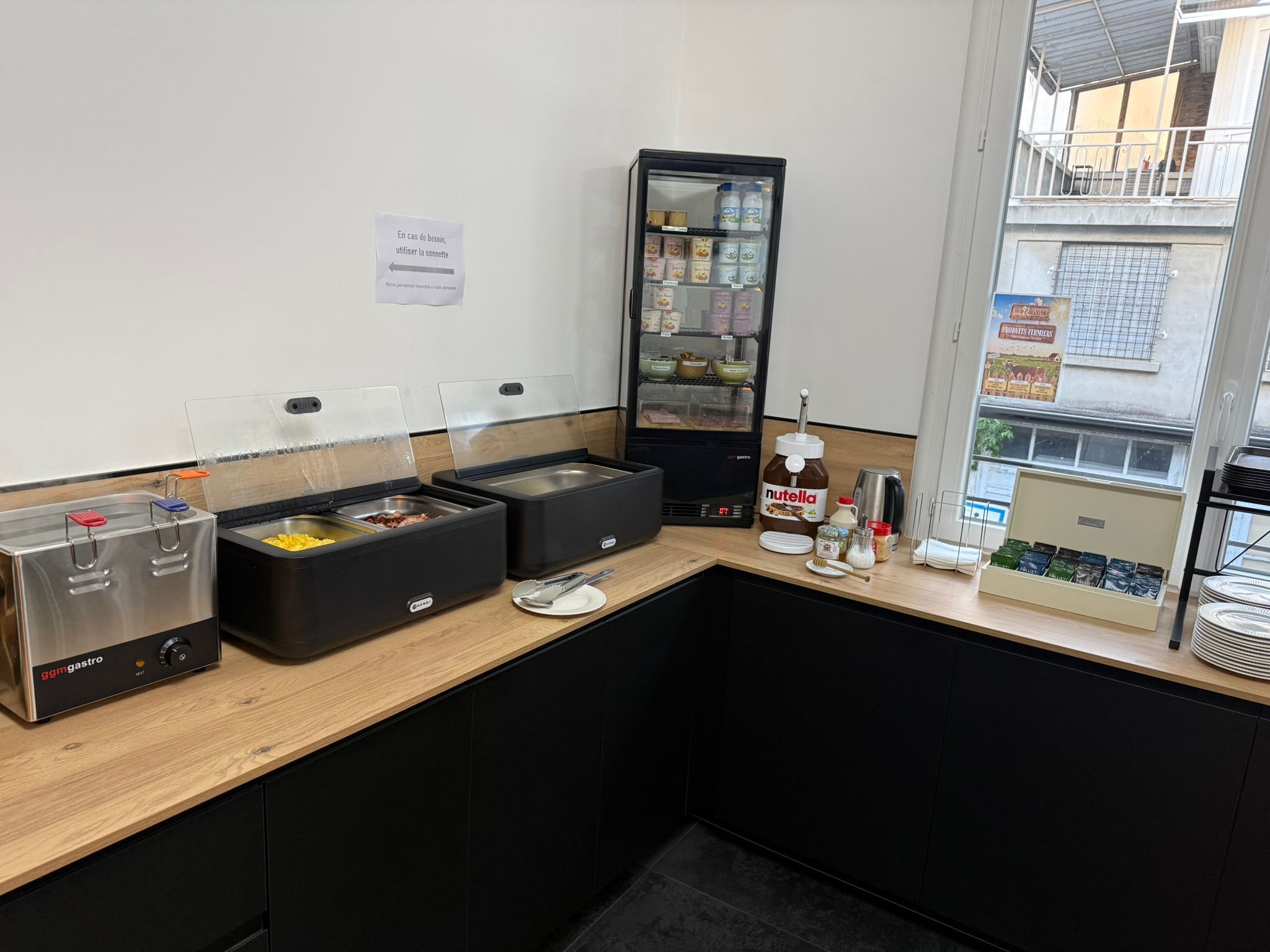 A kitchenette with a food warming station, a refrigerator, and a window with a view of buildings.