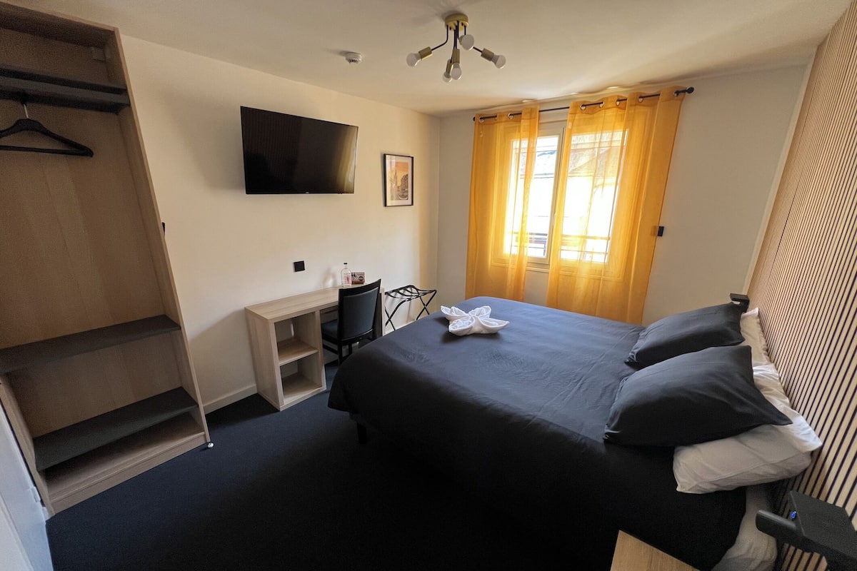 A hotel room with a bed, a desk, a chair, a TV, and a wardrobe.
