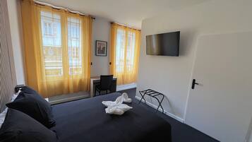 A hotel room with a bed, a desk, a chair, a TV, and a window with curtains.