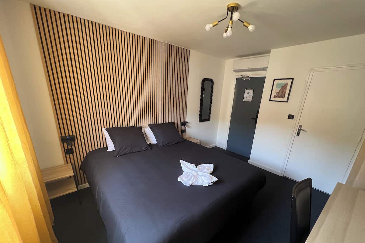 A hotel room with a large bed, a bedside table, a mirror, a door, and a wall with vertical stripes.