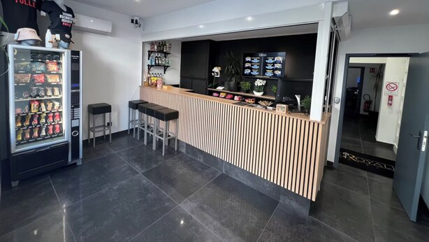 A modern bar area with a counter, stools, a beverage vending machine, and a digital menu display. - Hôtel Le Royal  (Tulle)