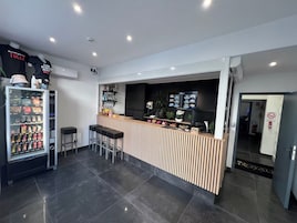 Uma área de bar moderna com balcão, banquetas, máquina de venda de bebidas e um painel digital de menu.
