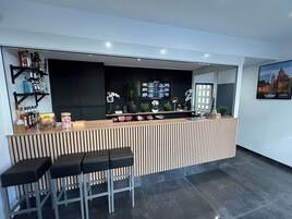 Uma área de recepção com balcão de madeira, banquetas pretas, uma televisão e um quadro pendurado na parede.