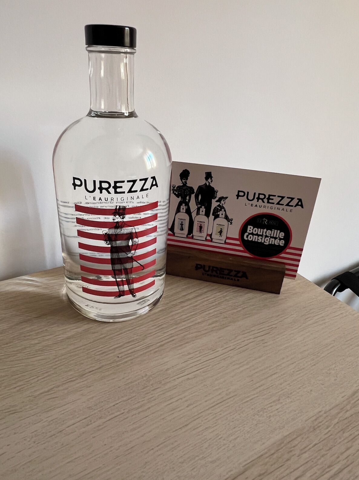Una bottiglia di Purezza l'eau originale e la sua confezione su una superficie di legno.