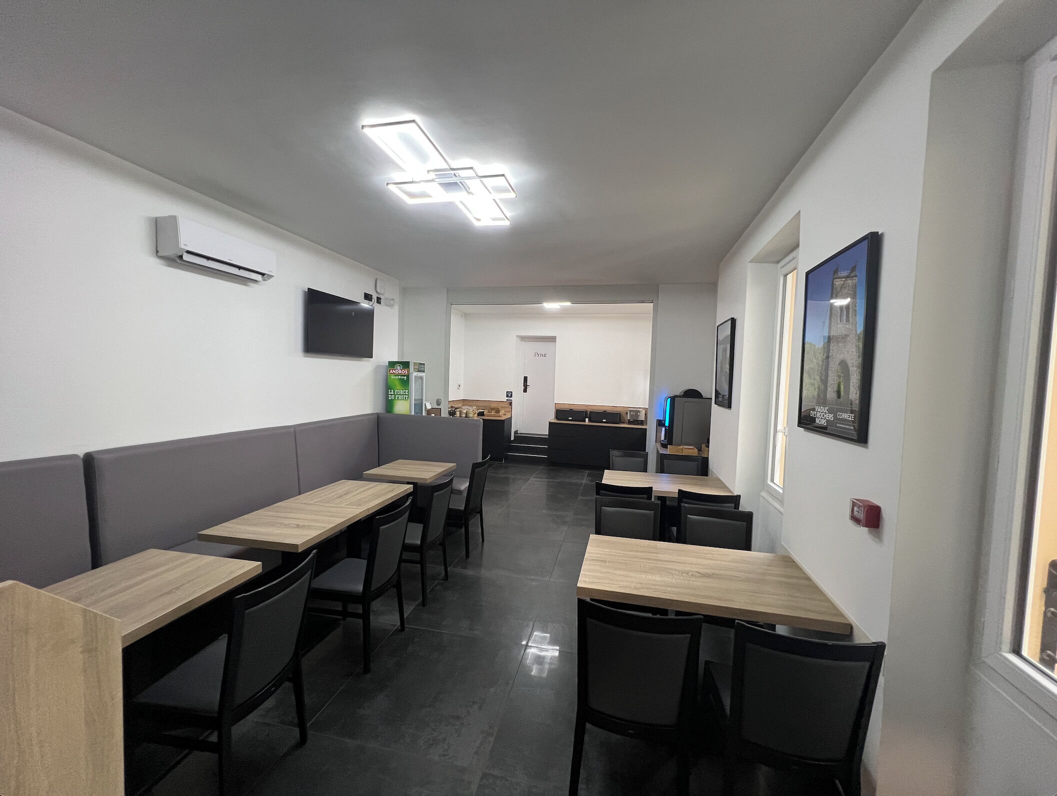 A modern dining area with booths and tables, a flat-screen TV mounted on the wall, and a window with a view of a building.