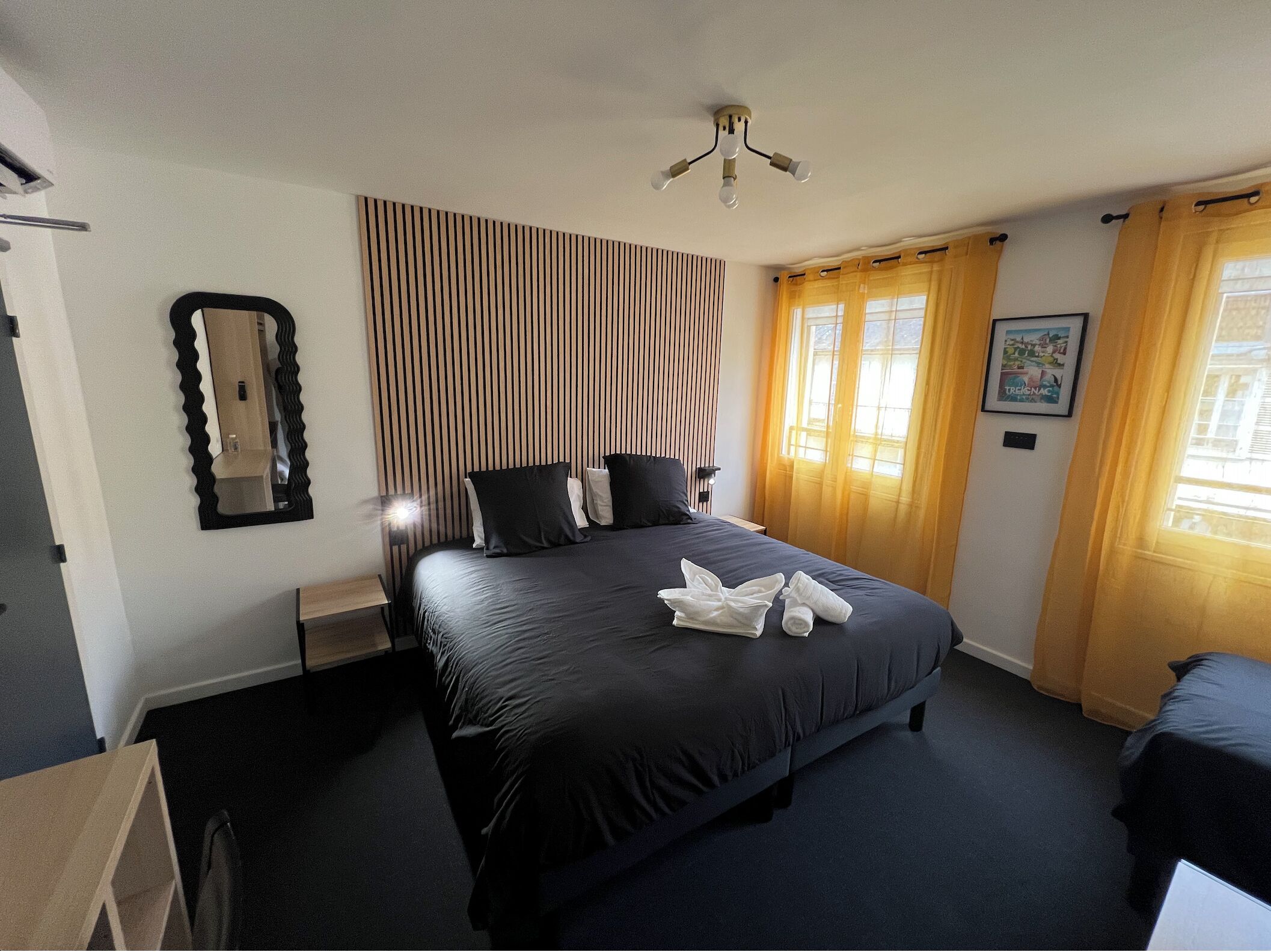 Una habitación de hotel con una cama grande, una mesita de noche, un espejo y un ventilador de techo.