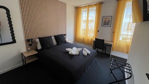 A hotel room with a bed, a desk, a chair, a mirror, and curtains. - Hôtel Le Royal  (Tulle)