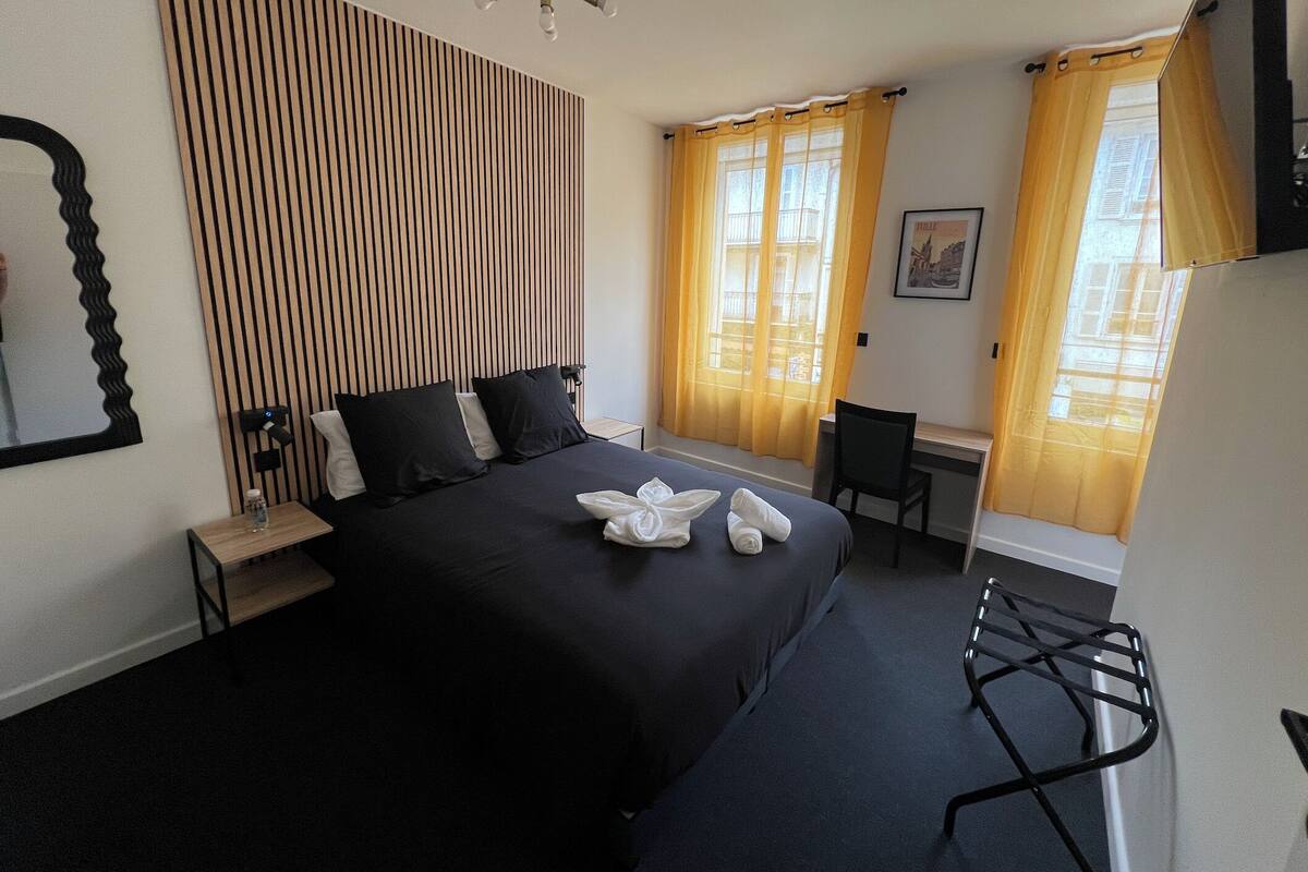 A hotel room with a bed, a desk, a chair, a mirror, and curtains.