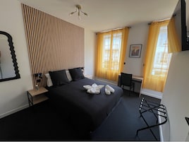 Quarto de hotel com cama, escrivaninha, cadeira, espelho e cortinas.