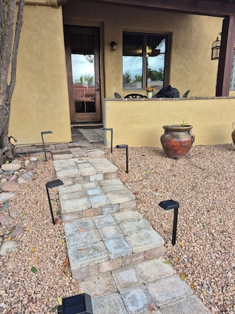 A stone pathway leading to a door, with a potted plant and a lantern on the right.