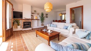 Una sala de estar con chimenea, sofás blancos, una mesa de centro de madera y una lámpara colgante.