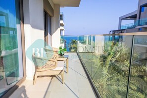 A balcony with wicker furniture, a potted plant, and a glass railing overlooking the sea. - Bloomfield 2BR Address Beach Resort (Al Aqah)