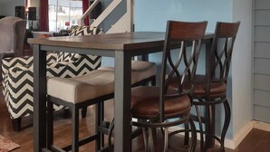 A dining area with a wooden table and four chairs, a clock on the wall, and a staircase in the background.