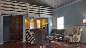 A spacious living room with a high ceiling, a sliding barn door, and a view into the kitchen area.
