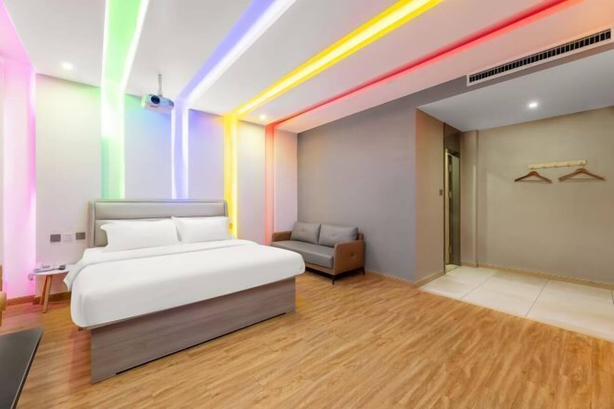 A modern hotel room with a large bed, a seating area, and a wardrobe with hangers.