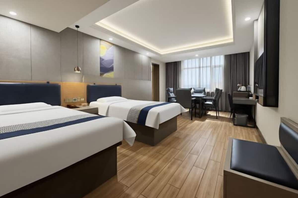 A hotel room with two beds, a desk, a chair, a TV, and a window.