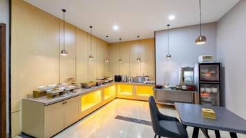 A modern kitchen with a dining area, featuring pendant lighting, a refrigerator, and a coffee machine.