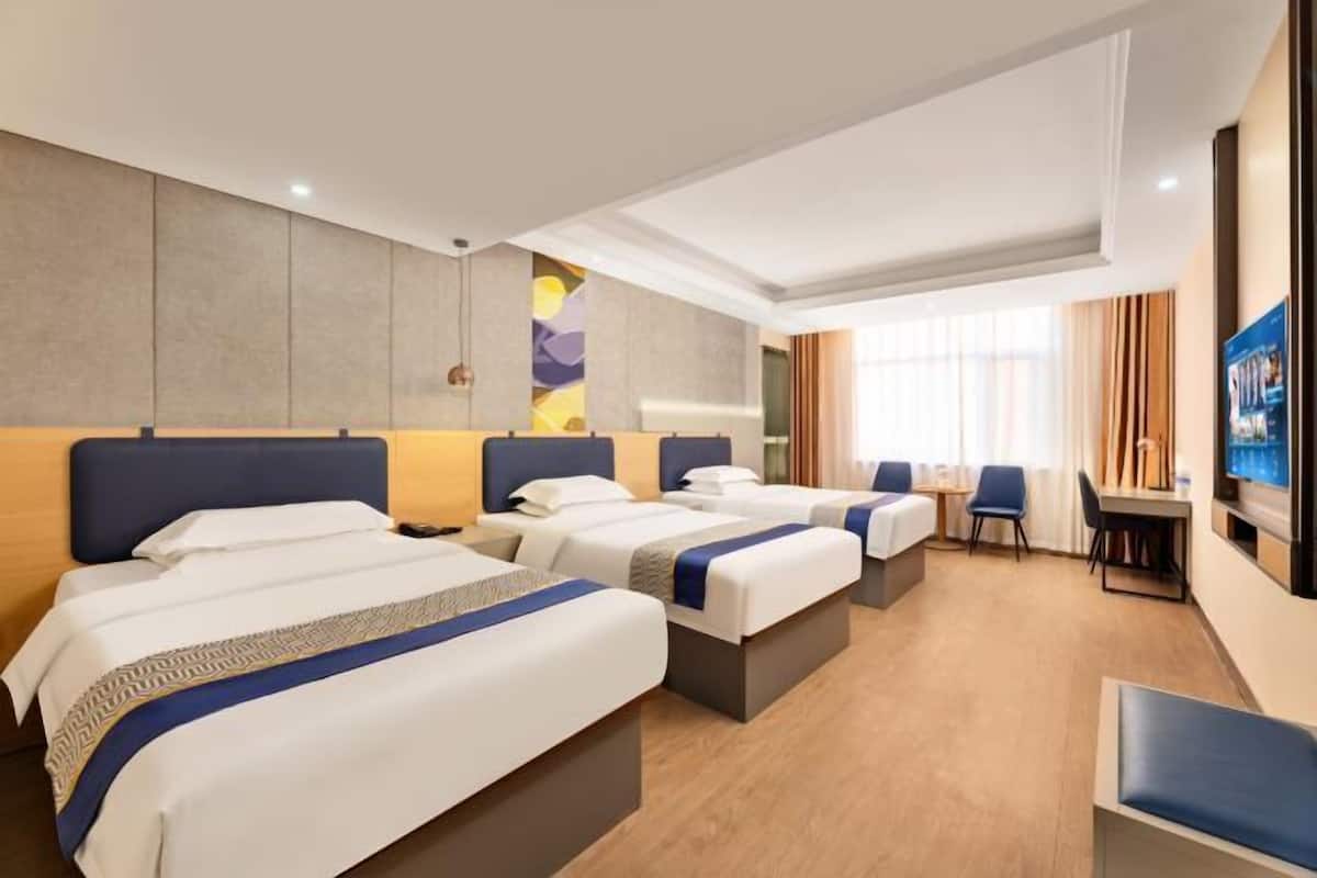 A hotel room with three beds, a desk, and a television.