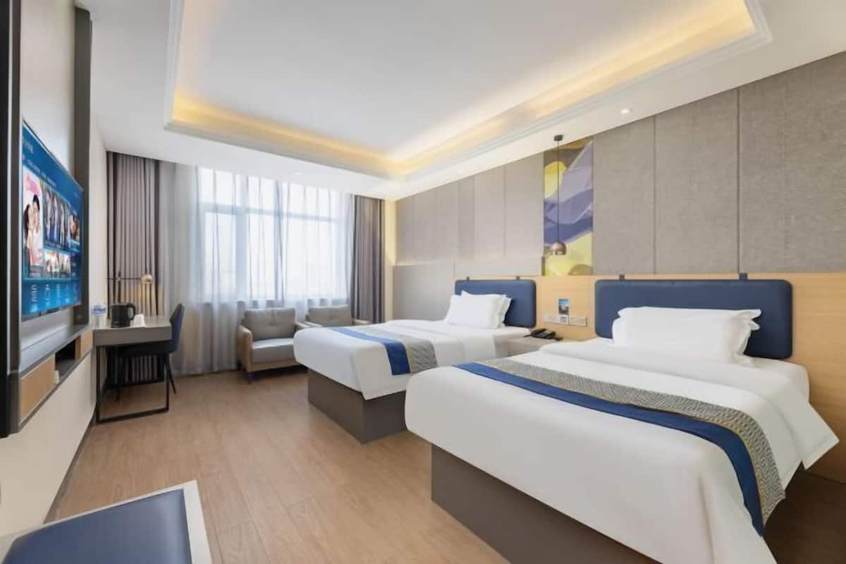 A hotel room with two beds, a desk, a chair, and a TV.