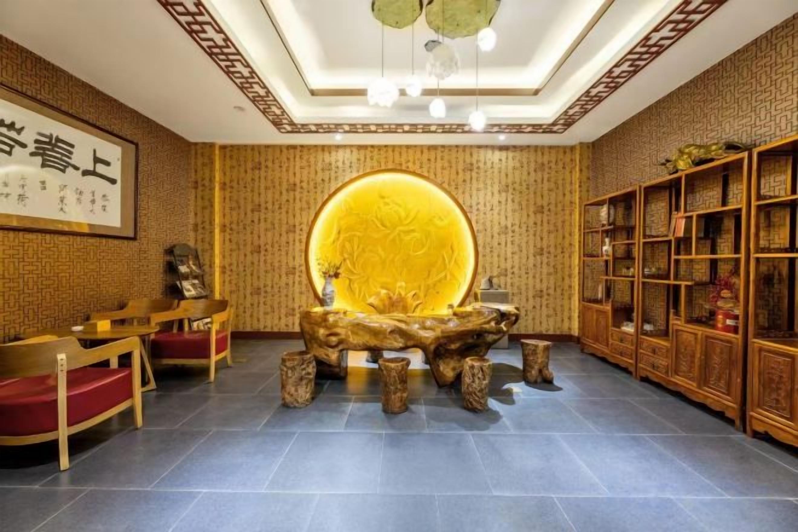 A traditional interior with a central wooden table, a bookshelf, and a framed artwork on the wall.