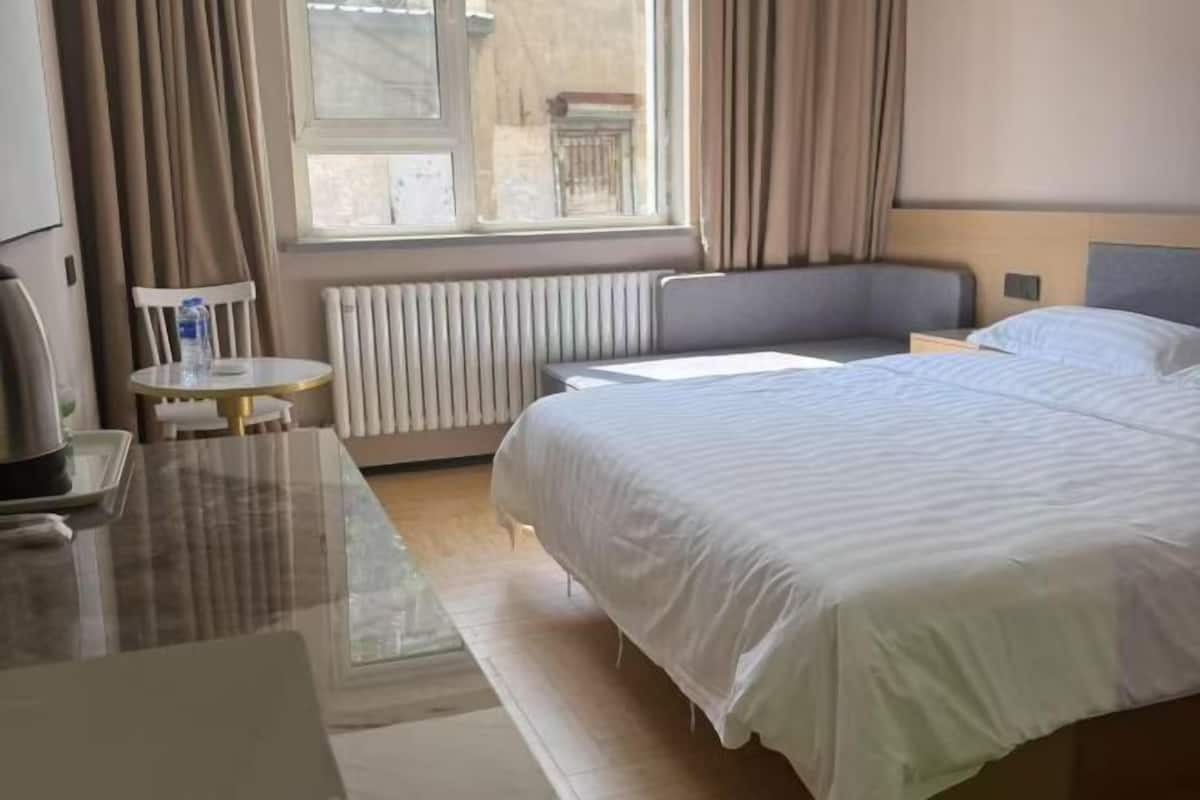 Habitación de hotel con cama, una mesita, una silla, radiador y ventana con cortinas.