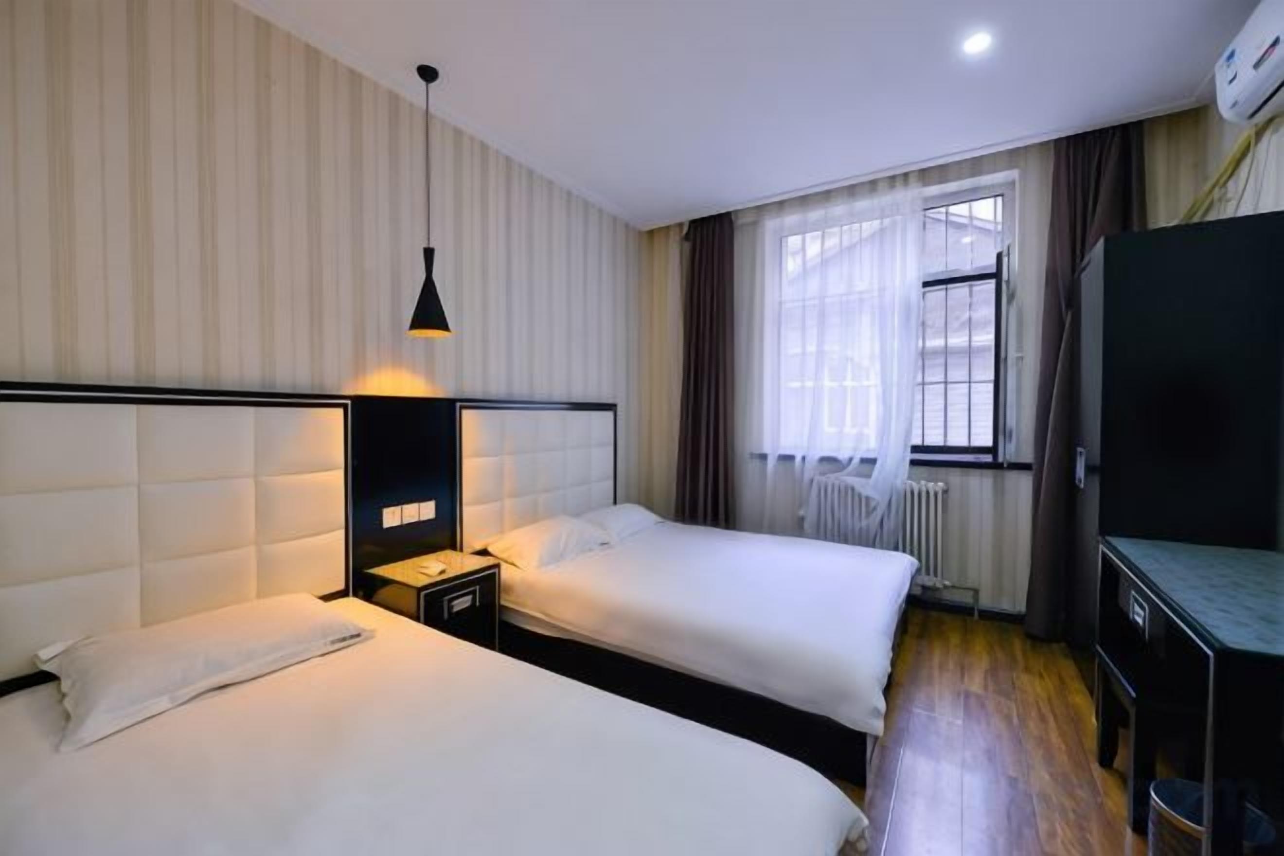 A hotel room with two beds, a bedside table, a lamp, a TV, and a window with curtains.