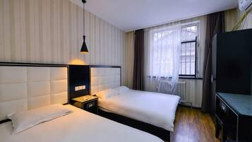 A hotel room with two beds, a bedside table, a lamp, a TV, and a window with curtains.