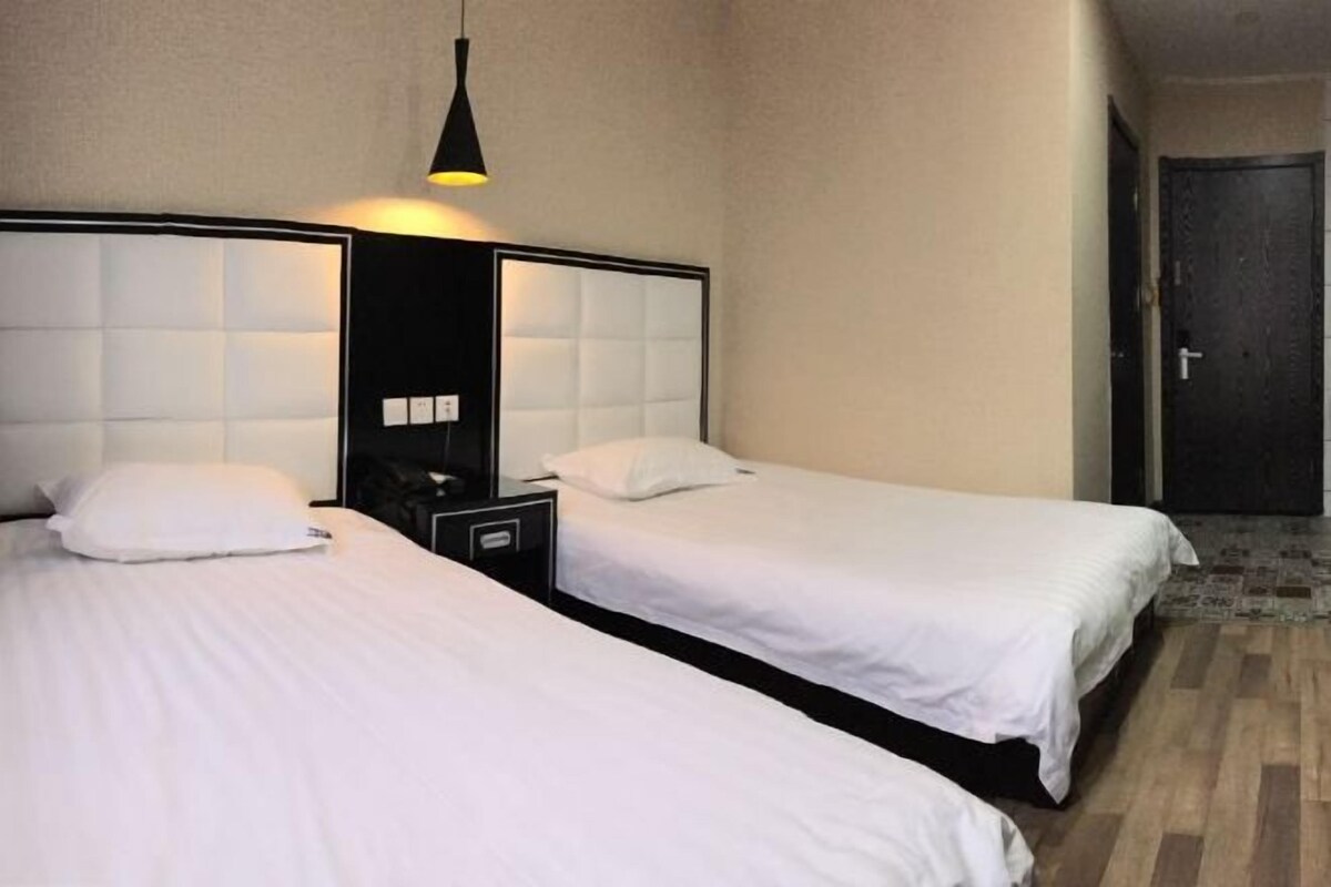 Two single beds with headboards, a bedside table, and a hanging light fixture in a hotel room.
