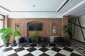 A lobby with a checkered floor, a brick wall, and seating area with plants. - Pebble Hotel (Dalian Xi'an Road Jiaotong University) (Dalian)