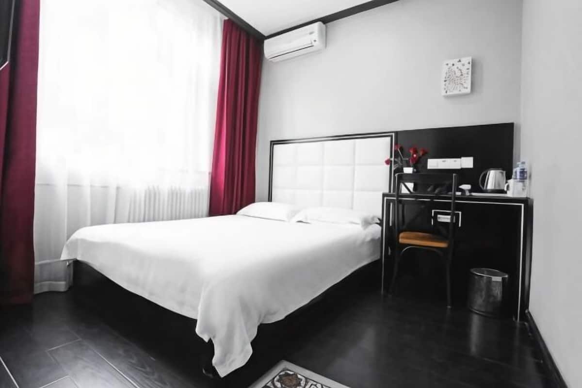 Una habitación de hotel con cama, escritorio, silla, cesto de basura y aire acondicionado instalado en la pared.