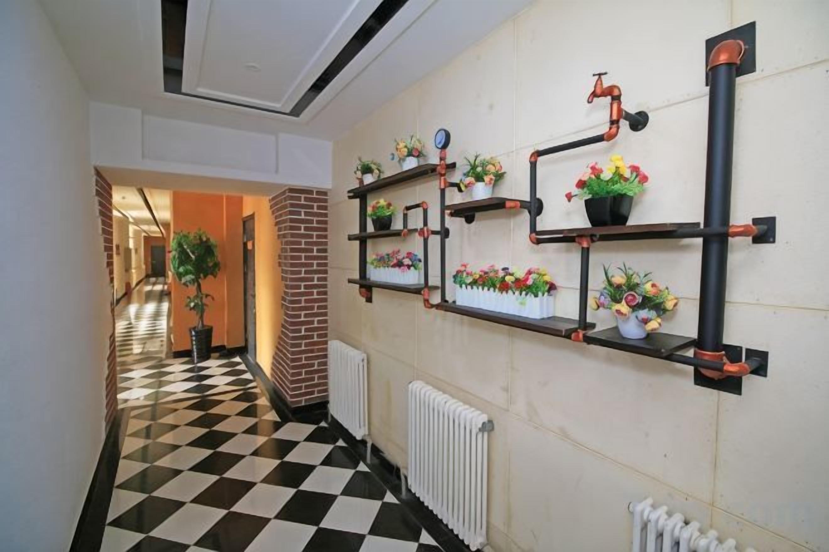 A hallway with checkered flooring, a brick wall, and metal shelving units with potted plants.