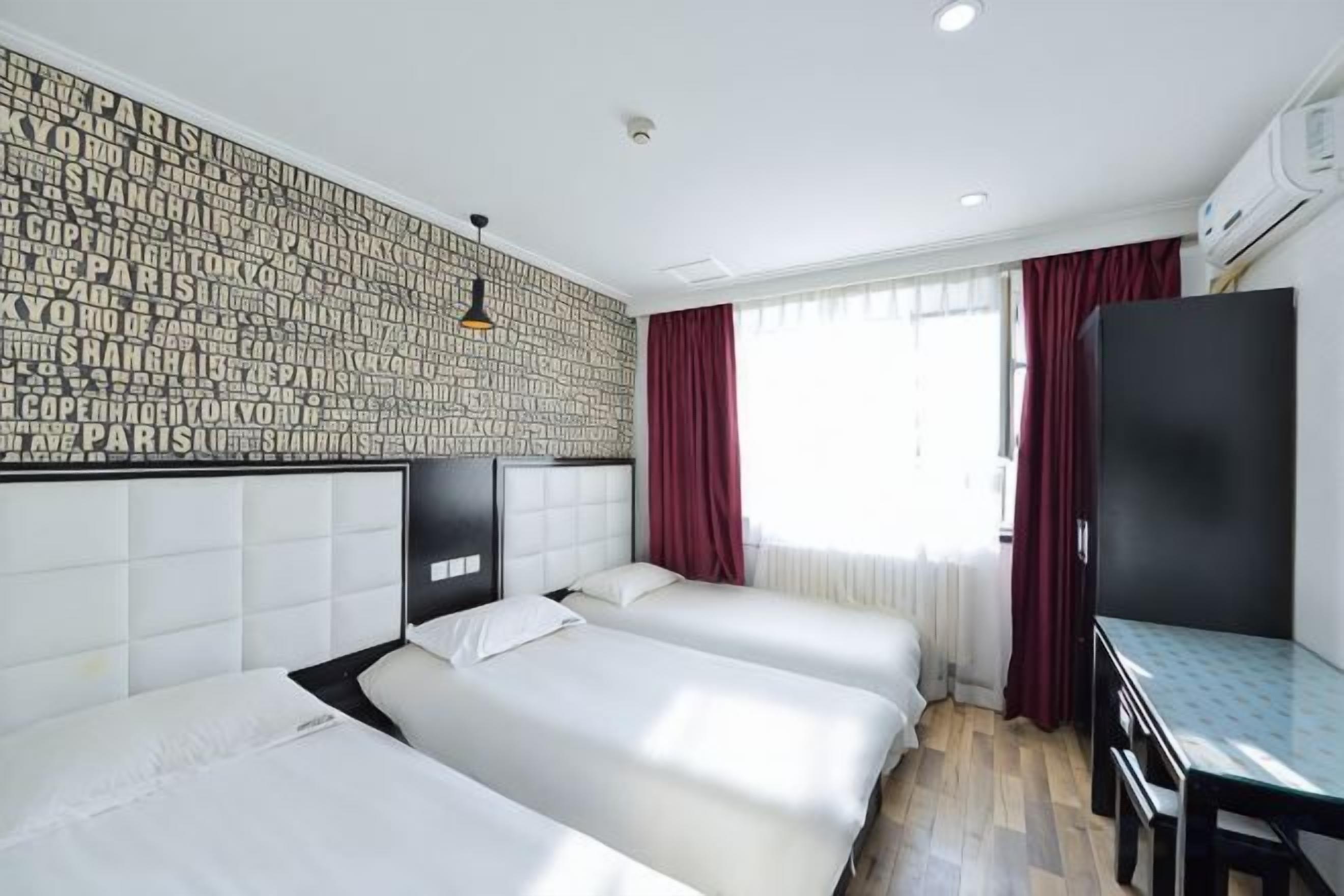 Quarto de hotel com três camas, uma escrivaninha e uma televisão.