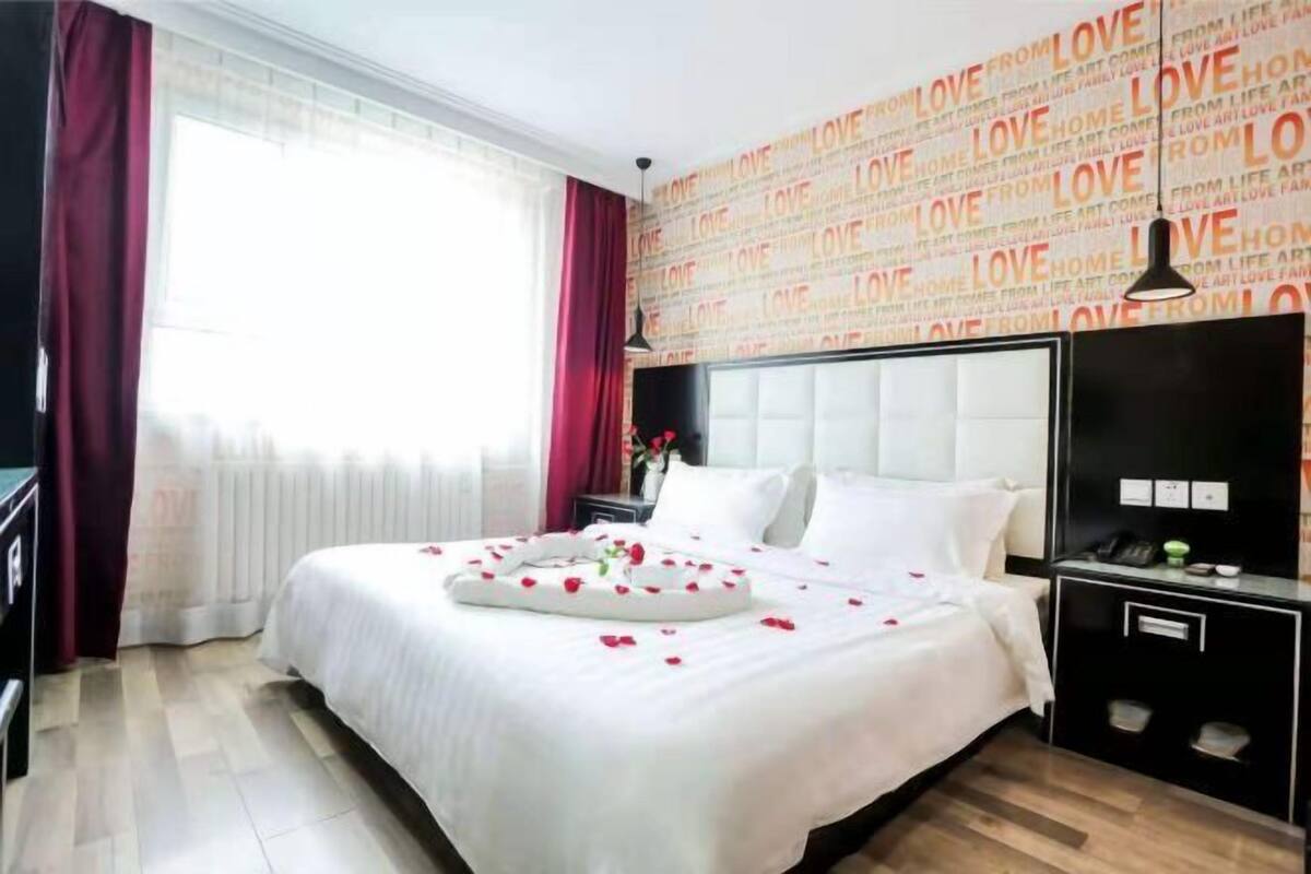 Una habitación de hotel con una cama grande, una mesita de noche, un escritorio y una pared con texto repetido.