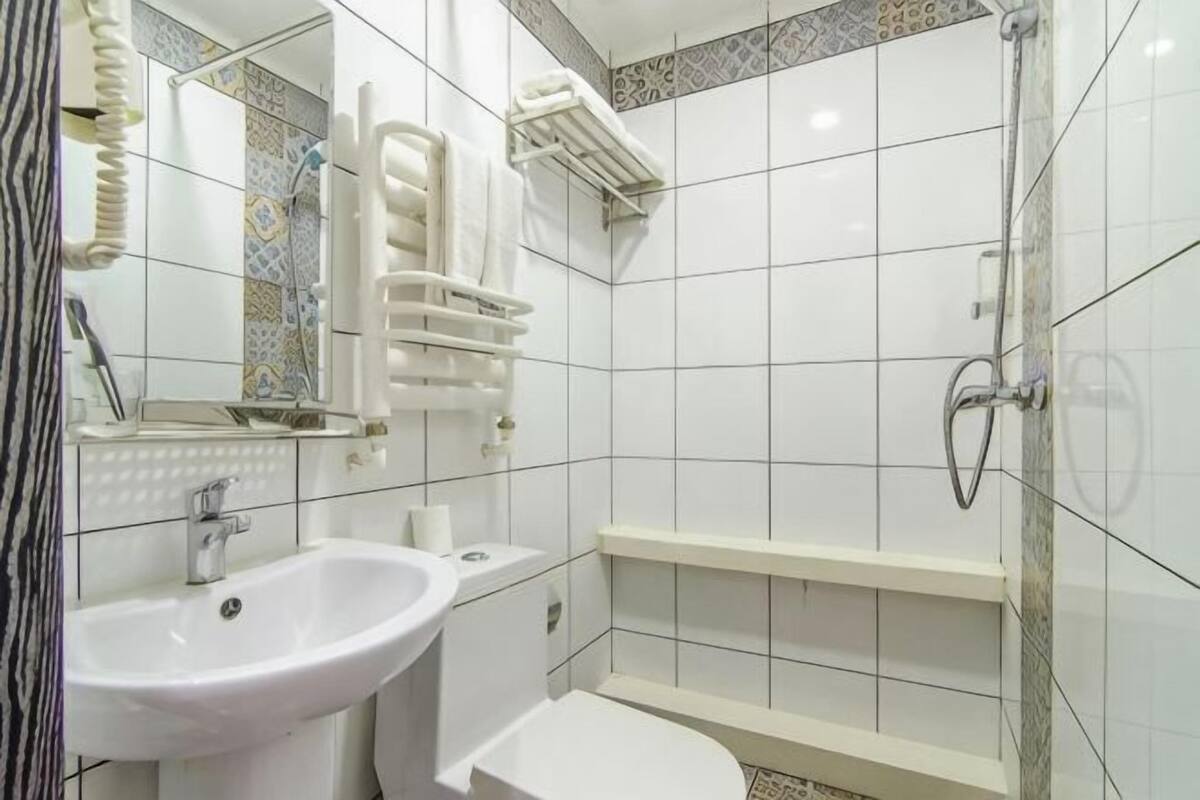 Un baño con lavamanos, espejo, toallero y ducha.