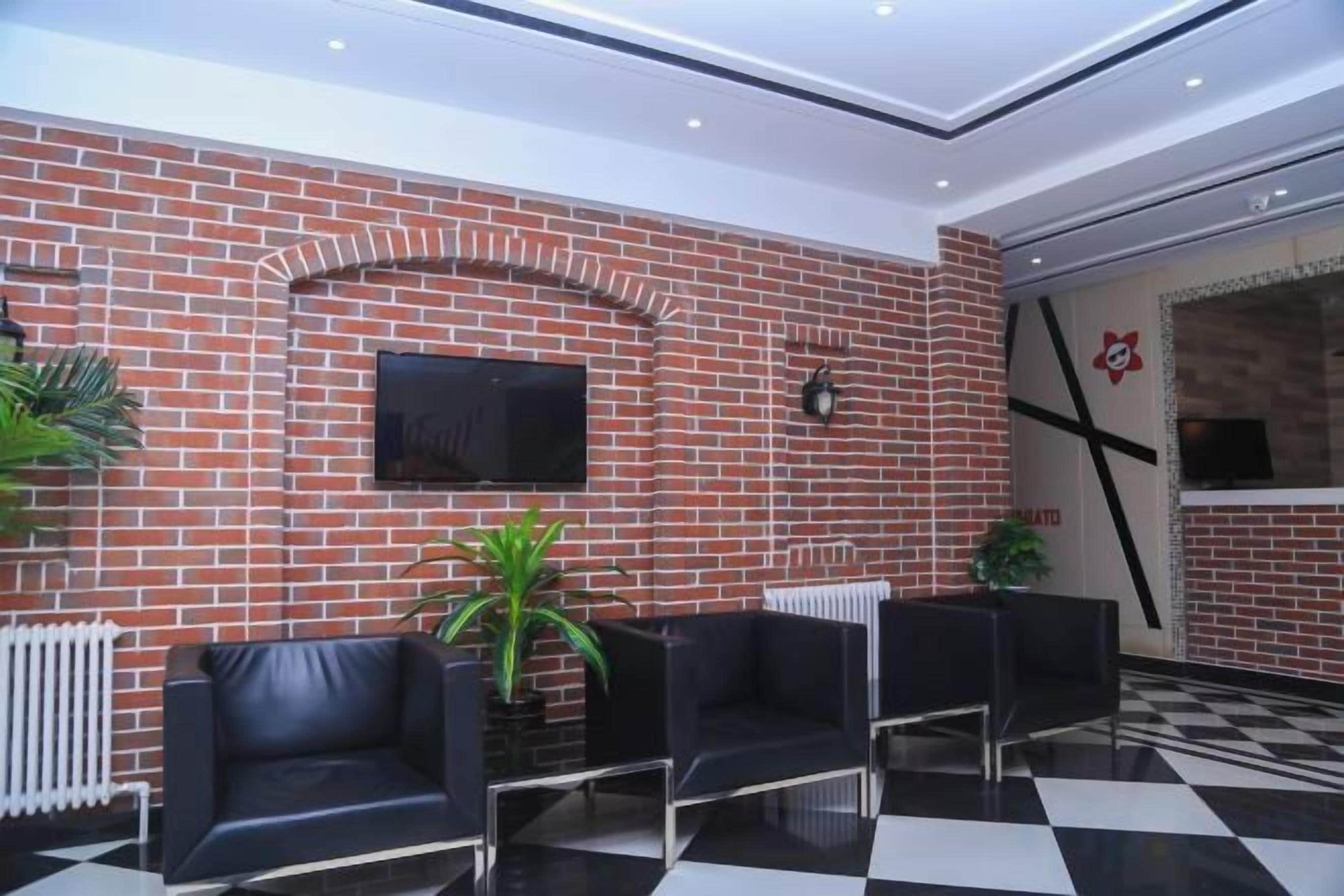 Un vestíbulo con pared de ladrillo, televisor de pantalla plana, sillas de cuero negro y suelo a cuadros.