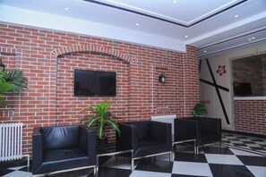 A lobby with a brick wall, a flat-screen TV, black leather chairs, and a checkered floor. - Pebble Hotel (Dalian Xi'an Road Jiaotong University) (Dalian)