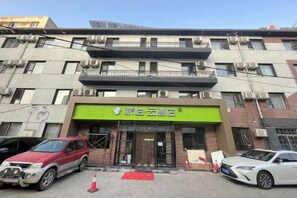 A building with a green sign, multiple floors, and parked cars in front. - Pebble Hotel (Dalian Xi'an Road Jiaotong University) (Dalian)