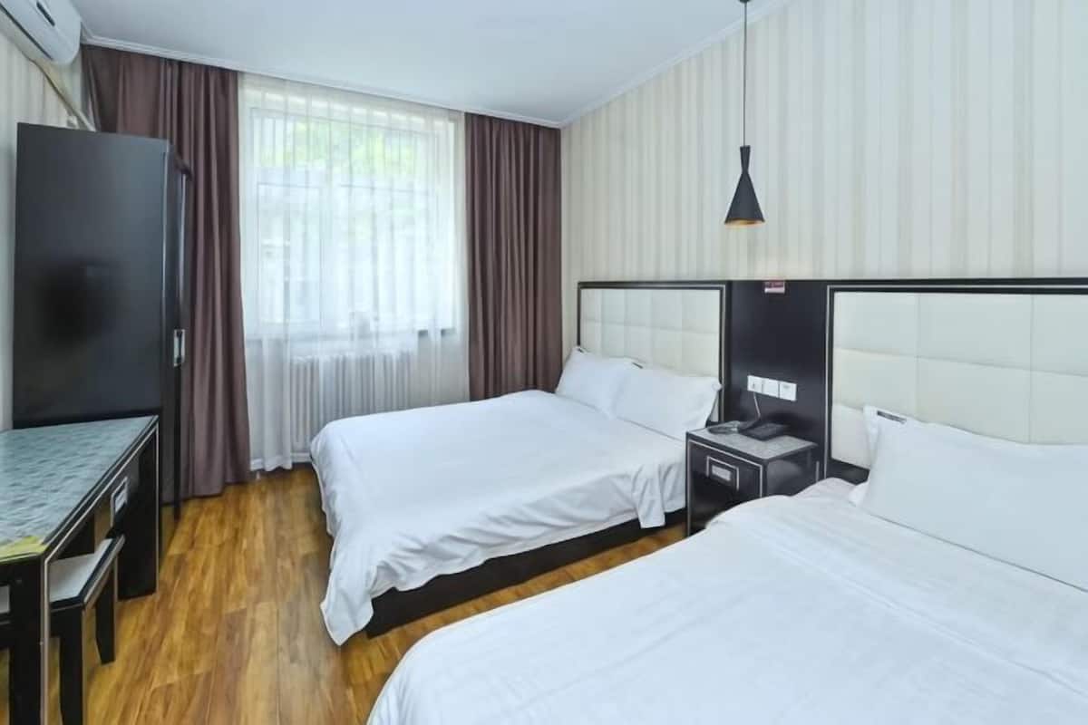 Habitación de hotel con dos camas, un escritorio, un televisor y una ventana con cortinas.