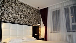 A hotel room with a large bed, a headboard with a city name pattern, a nightstand, and a window with sheer curtains. - Pebble Hotel (Dalian Xi'an Road Jiaotong University) (Dalian)