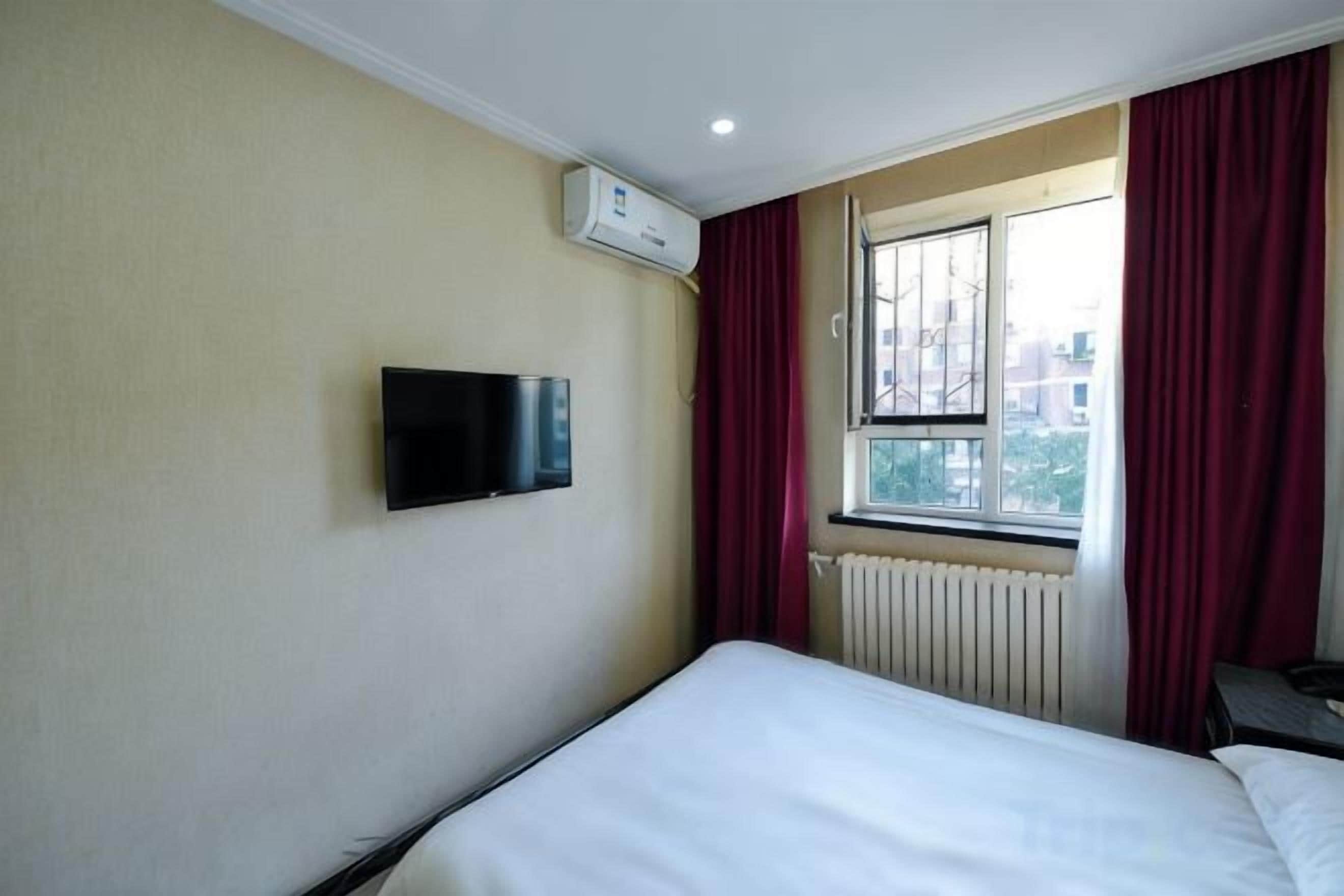 Une chambre d’hôtel avec un lit, un téléviseur fixé au mur, une fenêtre avec des rideaux et un radiateur.