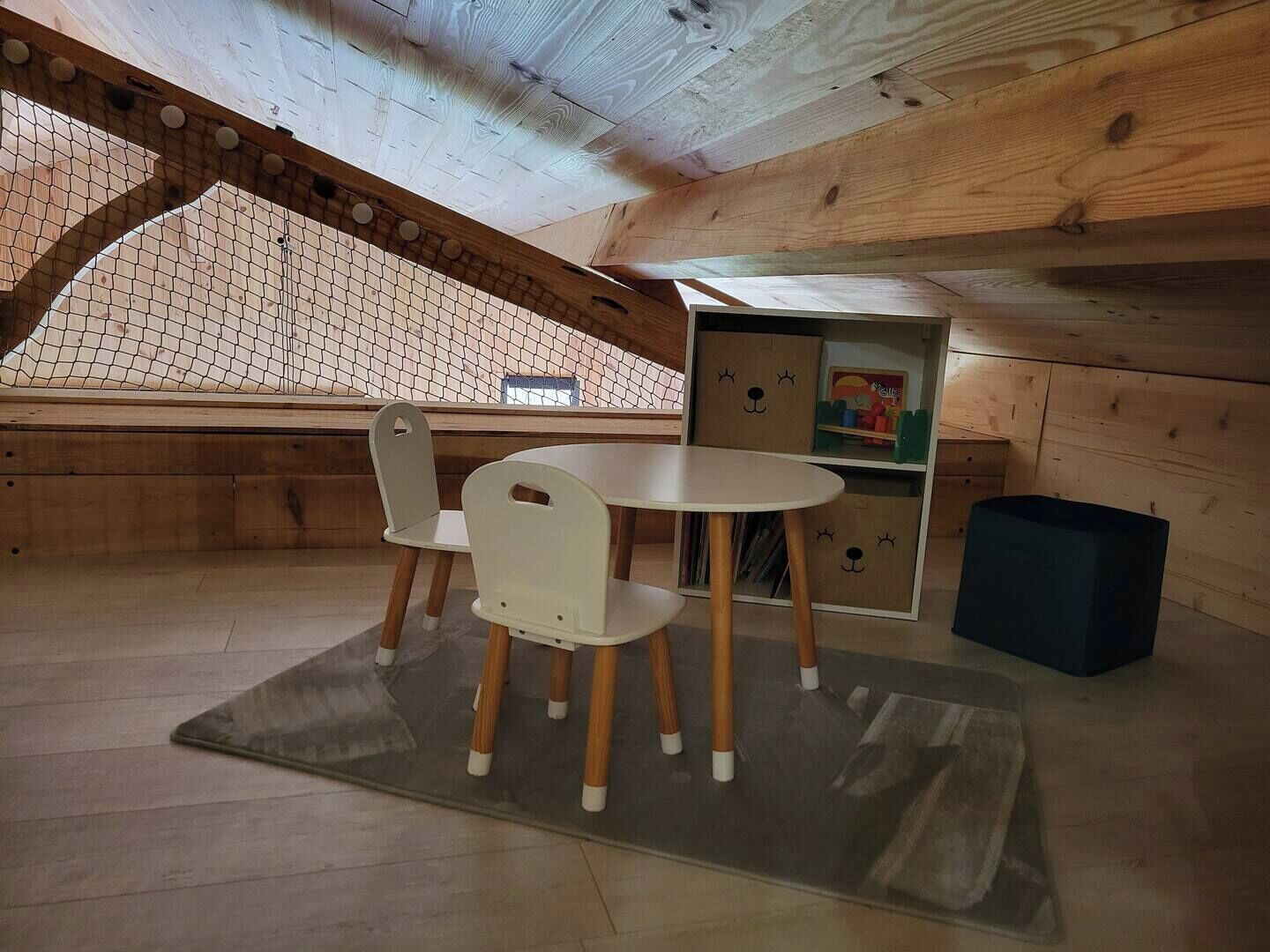 A cozy attic room with a wooden ceiling, a small table with chairs, and a bookshelf.