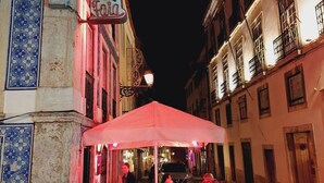 An outdoor dining area with tables and chairs under a canopy, a sign for a restaurant, and buildings with traditional architecture.
